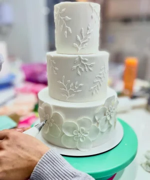 Bolo de casamento branco minimalista com flores artesanais sendo decorado pela Alegra Cakes em Florianópolis